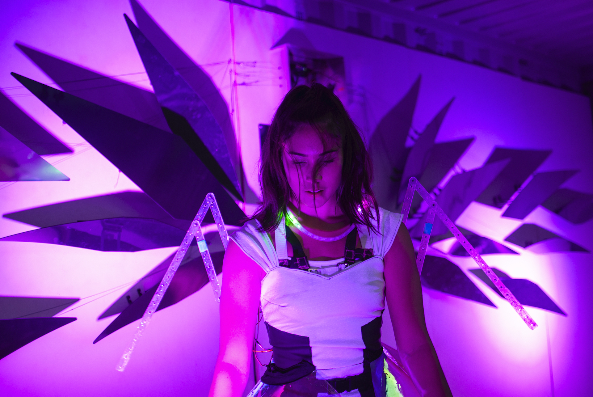 dancer performing and looking down, wearing a pair of strap on interactive robotic wings made of clear material