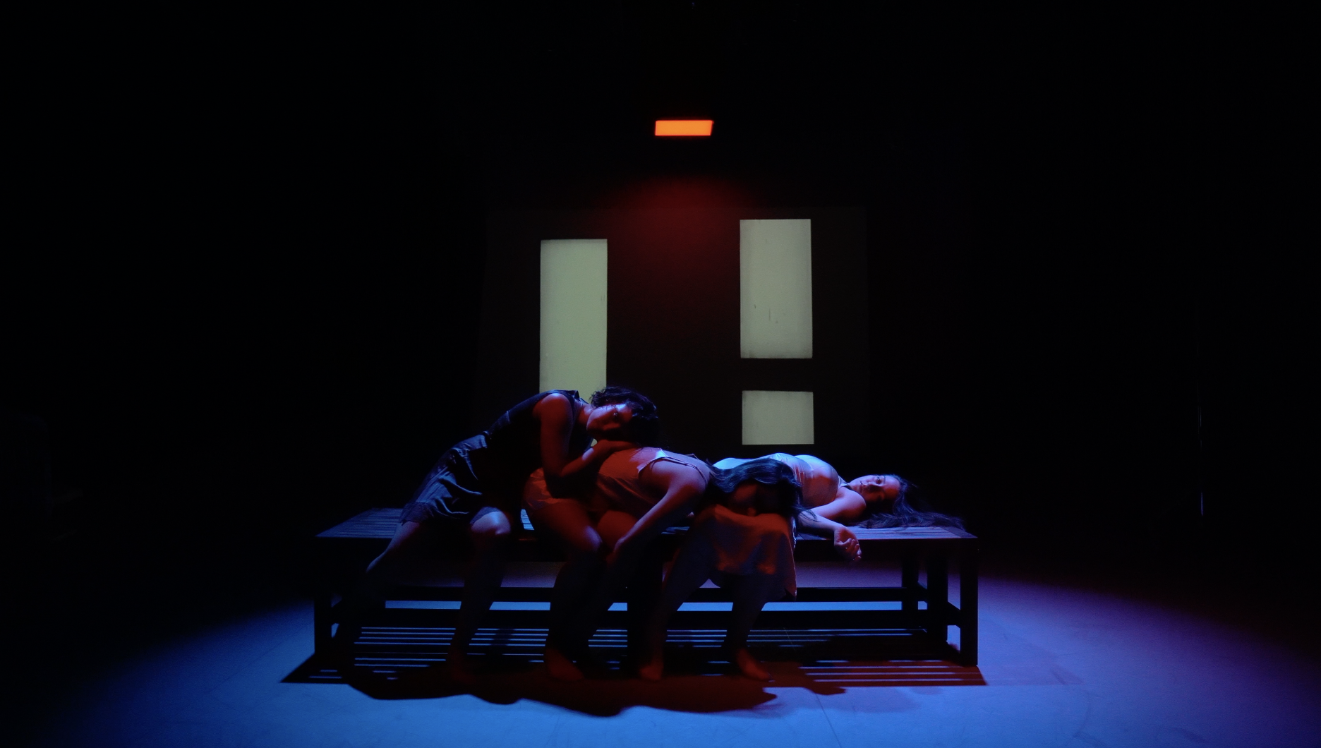 Three people leaning to the right on a bench lying on top of each other under colorful lights